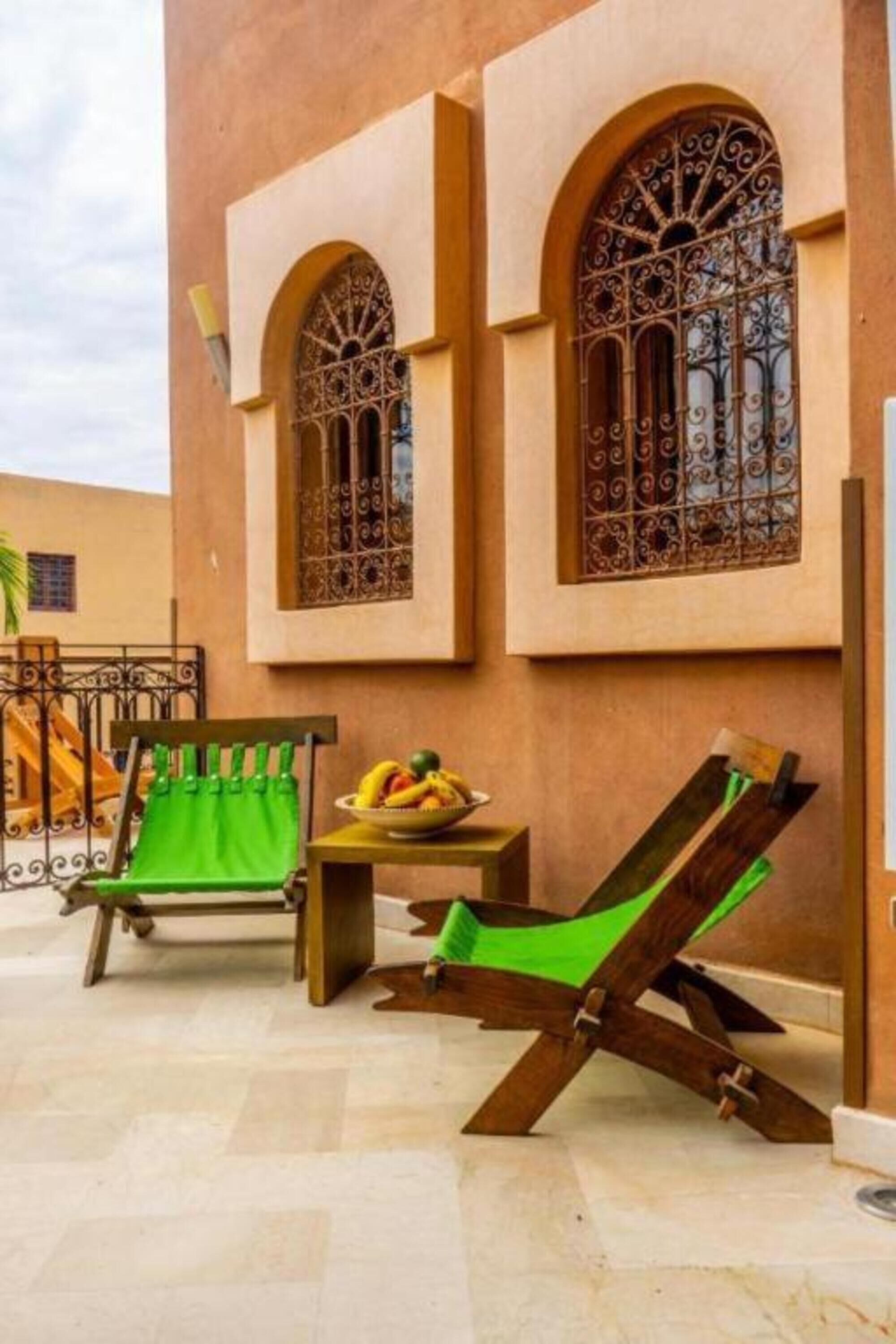 A courtyard with two green cushioned chairs, a small table with fruit, and a decorative metal gate.