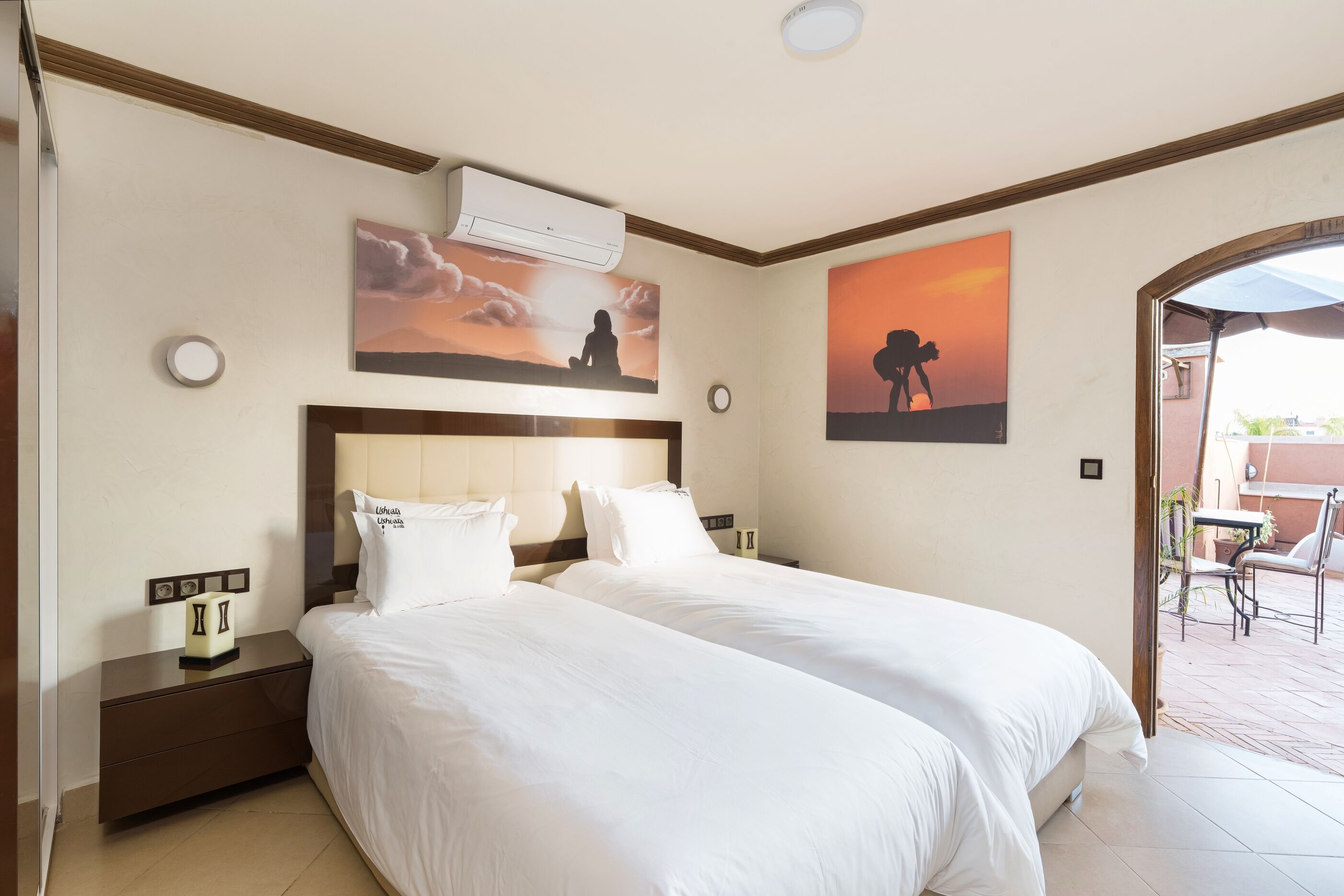 Une chambre d’hôtel avec deux lits, une table de chevet, un climatiseur et des œuvres d’art représentant un coucher de soleil.