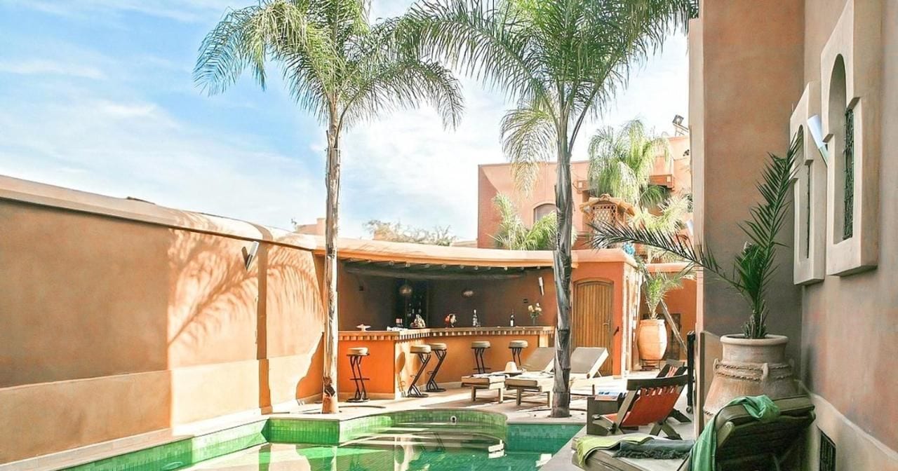 A pool area with lounge chairs, a bar, and palm trees.