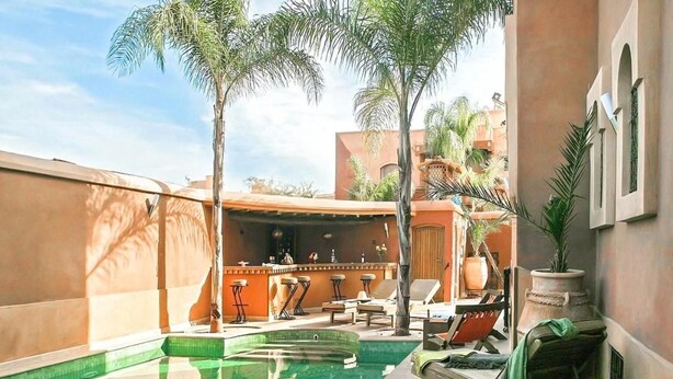 A pool area with lounge chairs, a bar, and palm trees. - Riad Ushuaia la Villa - Centre Marrakech (Marrakech)