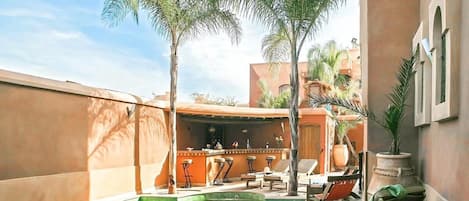 A pool area with lounge chairs, a bar, and palm trees.