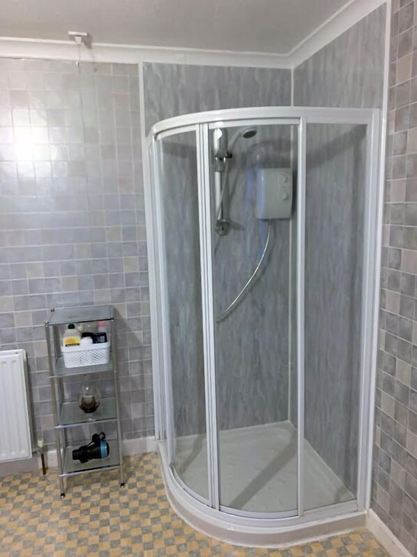 A shower with a glass door, a white radiator, and a checkered floor. - Dunrigh Guest House (Oban)