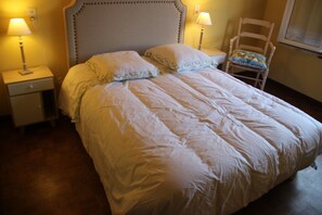 Una cama bien hecha con un cabecero, dos lámparas de noche, una silla y una mesita de noche.