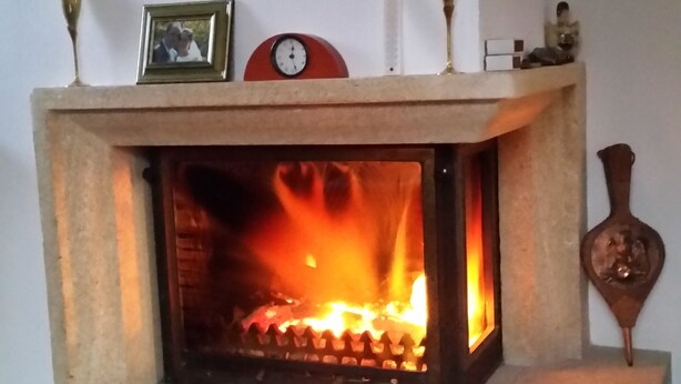 A fireplace with a fire, surrounded by a stone hearth, a clock, and a framed picture on the mantel. - Chambres d'hôtes Elisa & Etienne (Manosque)