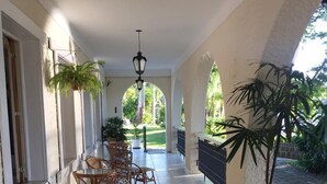 A covered outdoor area with a tiled floor, a patterned rug, potted plants, wicker furniture, and a hanging lantern. - Hotel Itamaracá (Miguel Pereira)