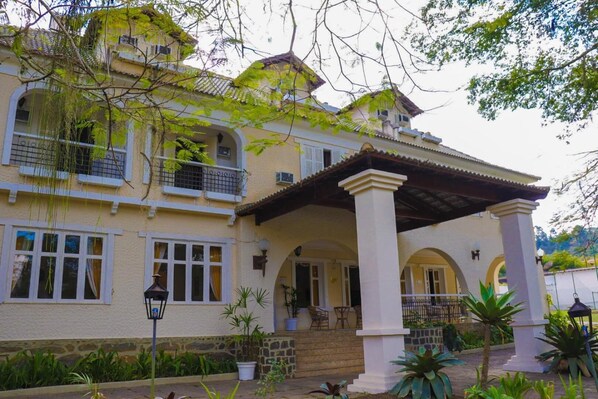 A two-story building with a balcony, a covered porch, and a stone wall.