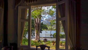 A room with a large window overlooking a lake and greenery. - Hotel Itamaracá (Miguel Pereira)