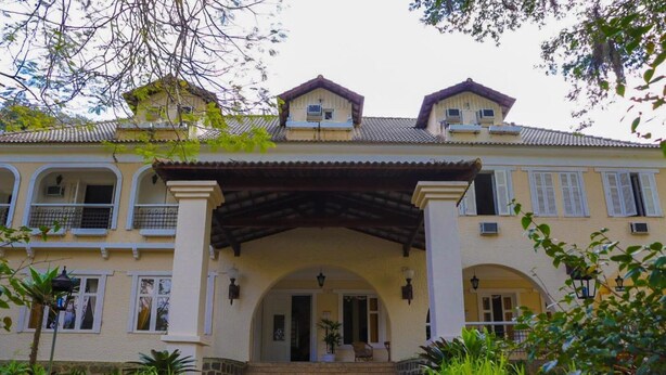 A two-story building with a central entrance, arched doorways, and a covered porch. - Hotel Itamaracá (Miguel Pereira)