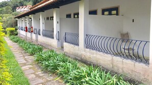 Filas de edificios blancos con tejados rojos y barandillas azules, rodeados de vegetación y un sendero de piedra.