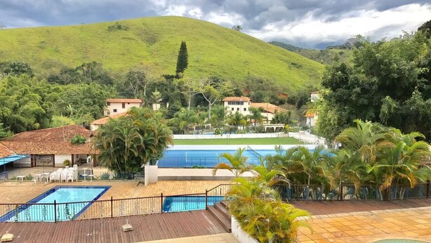 Un resort con varias piscinas, una terraza de madera y vistas a una colina con casas al fondo.