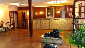 Un vestíbulo con paneles de madera, un mostrador de recepción, un reloj y una zona de estar con sillas y una mesa.