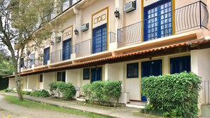 Una hilera de edificios blancos con puertas y ventanas azules, rodeados de follaje.