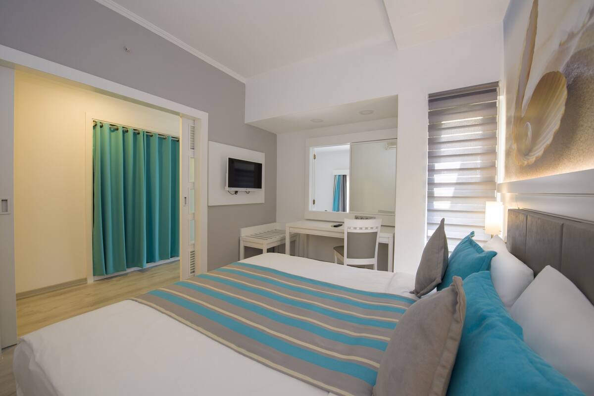 A hotel room with a bed, a desk, a chair, a television, and a large mirror.