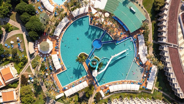 An aerial view of a resort with multiple swimming pools, palm trees, and a variety of sun loungers and umbrellas.