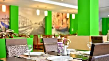 Un comedor con paredes verdes, un mural y mesas ordenadas con platos, vasos y cubiertos.
