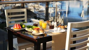 Une table à manger avec des aliments pour le petit-déjeuner, un verre de jus d’orange et une vue sur un port de plaisance.
