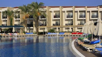 Una piscina con sillas de descanso y sombrillas, rodeada por un edificio de varios pisos con balcones.