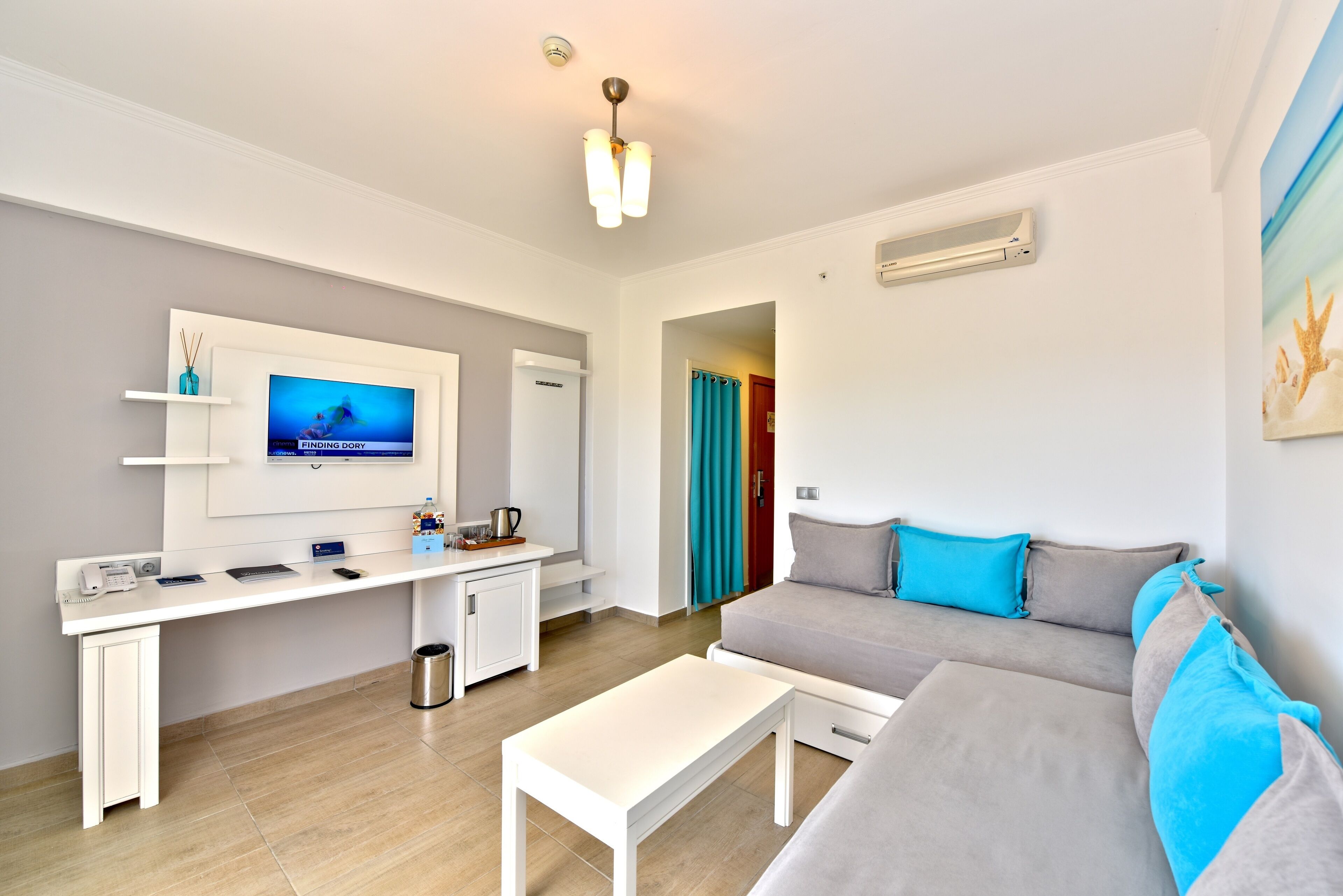 Una sala moderna con un televisor de pantalla plana, un sofá, una mesa de centro y un escritorio con una computadora y un teléfono.
