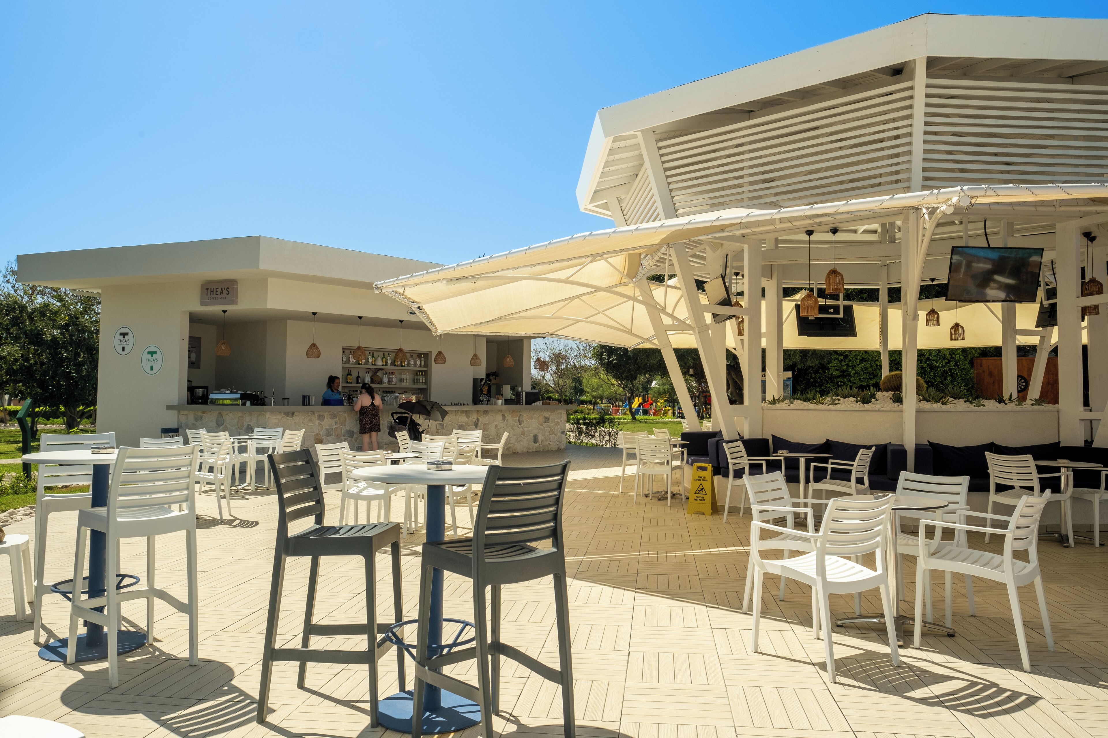 An outdoor patio area with white tables and chairs, a bar area, and a covered seating area with a TV screen.