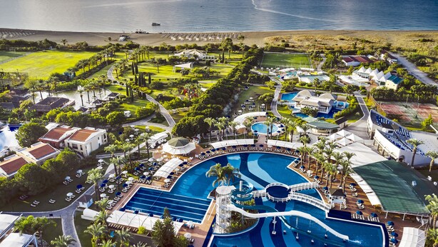 Vista aérea de un resort con múltiples piscinas, una playa y abundante vegetación.
