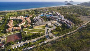 An aerial view of a resort with a swimming pool, tennis courts, and a beach.