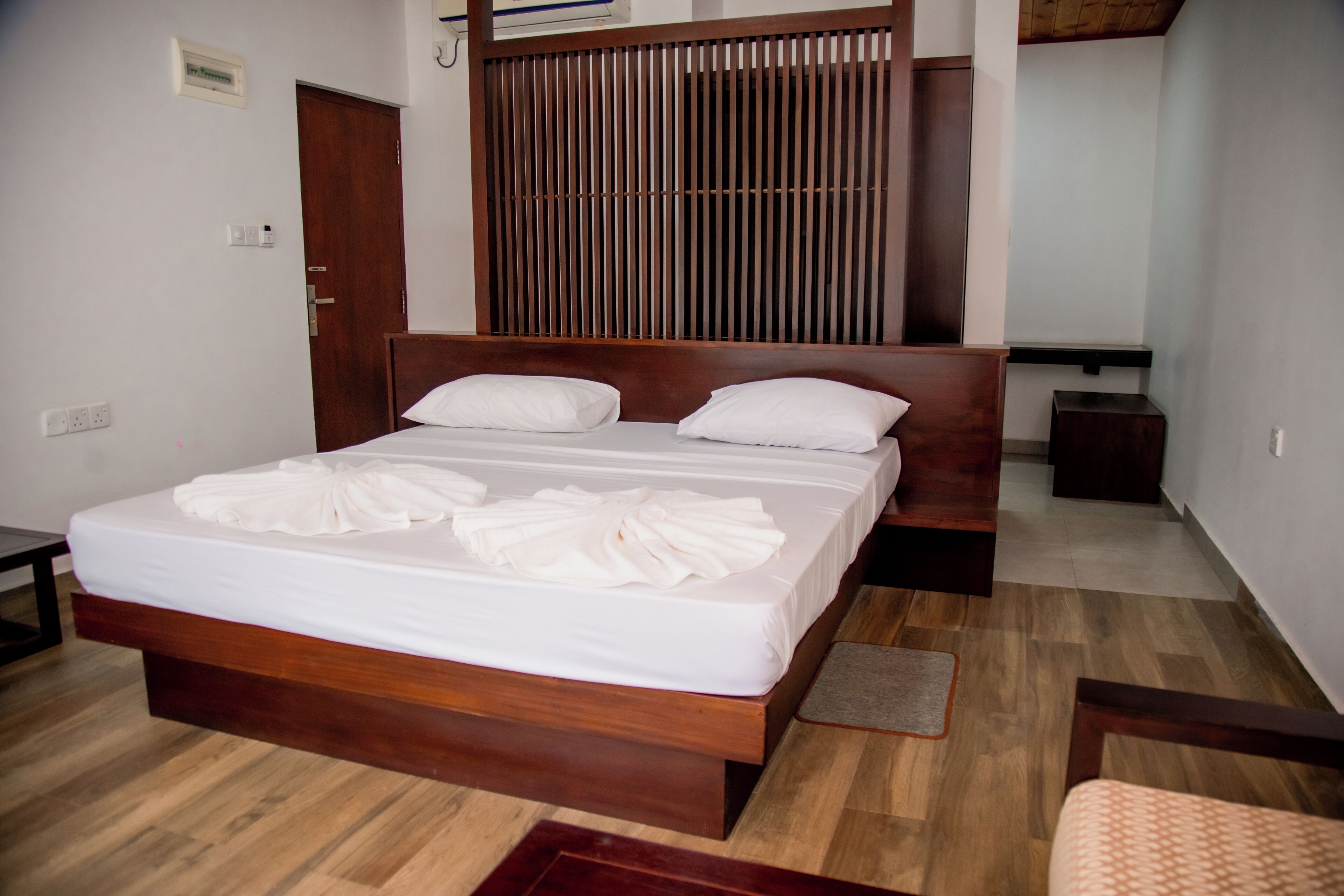 A neatly made bed with white linens and a wooden headboard, a wooden floor, and a small bedside table.