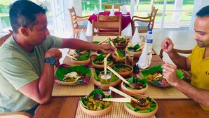 A dining table with multiple bowls of food and drinks, surrounded by wooden chairs. - Lavendish Wild Safari Resort (Maraka)