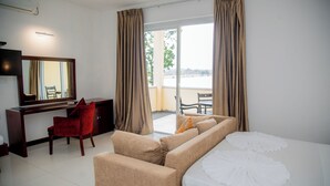 A hotel room with a bed, a desk, a red chair, a sofa, and a balcony with a view. - Lavendish Wild Safari Resort (Maraka)
