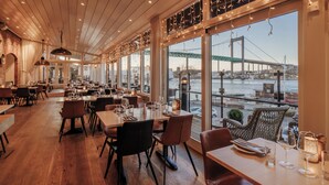 A restaurant with wooden floors, tables set for dining, and large windows offering a view of a bridge and water. - Quality Hotel Waterfront, Goteborg (Gothenburg)