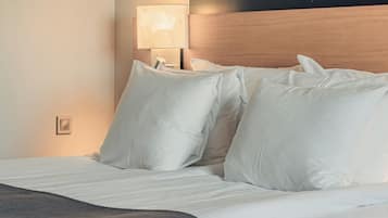 Una cama bien arreglada con sábanas y almohadas blancas, un cabecero de madera y una lámpara de noche con un motivo de hojas.
