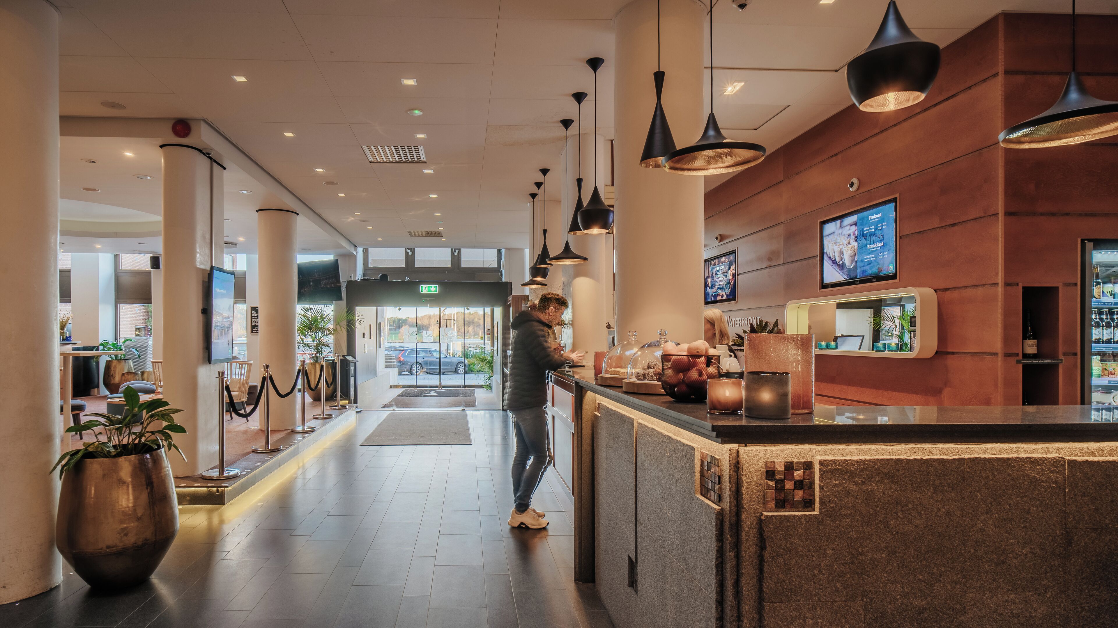 En modern hotellobby med en receptionsdisk, en sittgrupp och ett stort fönster med utsikt över gatan.