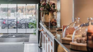 A hotel reception area with a glass door leading outside, a vase with flowers on the counter, and a display case with items.