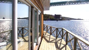 A wooden deck with glass doors leading to a river view, a metal railing, and a bridge in the background. - Quality Hotel Waterfront, Goteborg (Gothenburg)