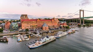 A large hotel with multiple red-roofed buildings, a dock with boats, and a bridge in the background. - Quality Hotel Waterfront, Goteborg (Gothenburg)