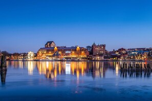 Un paisaje urbano frente al mar, con edificios iluminados que se reflejan en aguas tranquilas.
