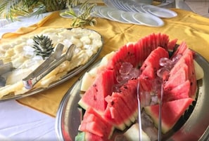 A table with a yellow tablecloth, two metal plates with food, and white plates in the background.