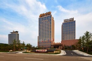Un hotel de varios pisos con entrada central, zona de estacionamiento y patio ajardinado.