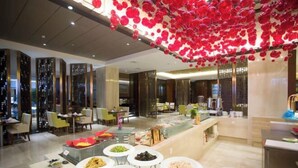 A hotel lobby with a buffet area featuring various dishes, a seating area with chairs, and a decorative ceiling with hanging ornaments. - Huaxi Hotel (Weihai)