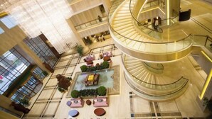 A multi-level atrium with a central spiral staircase, glass railings, and seating areas with plants. - Huaxi Hotel (Weihai)