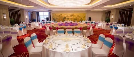 A banquet hall with round tables, white chairs, and a red carpet.