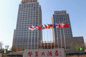 A hotel with multiple flags, including the American flag, in front of tall buildings. - Huaxi Hotel (Weihai)