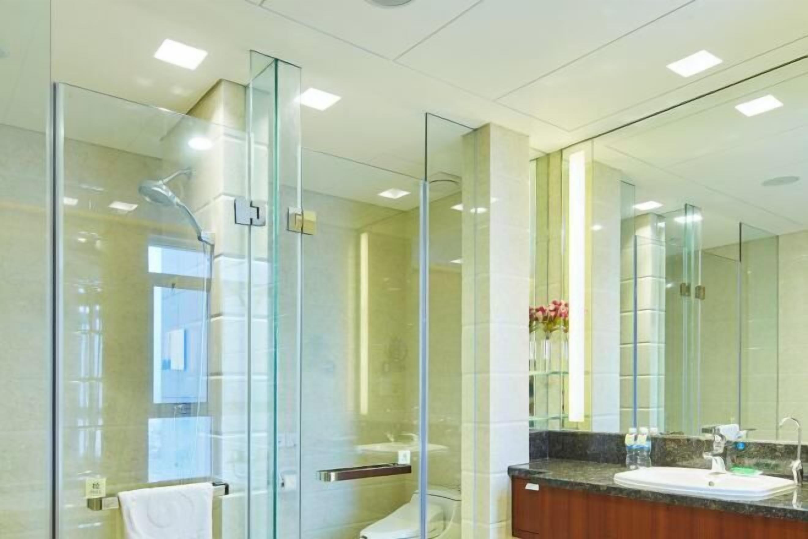 Un baño moderno con ducha envuelta en vidrio, tocador con lavamanos y un espejo grande.