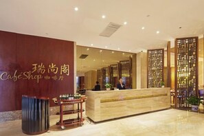 A hotel reception area with a reception desk, a trash bin, and a decorative wall with a sign. - Huaxi Hotel (Weihai)