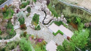 A landscaped garden with a central stone pathway, surrounded by various plants and rocks. - Huaxi Hotel (Weihai)
