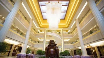 Un hall d’hôtel à plusieurs niveaux, doté d’un lustre central, de hauts plafonds et d’une grande statue.