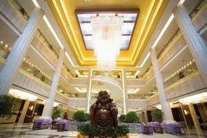 Vestíbulo de hotel de varios niveles con una araña central, techos altos y una estatua grande.