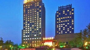 A high-rise hotel with multiple floors, illuminated windows, and a prominent sign at the top. - Huaxi Hotel (Weihai)