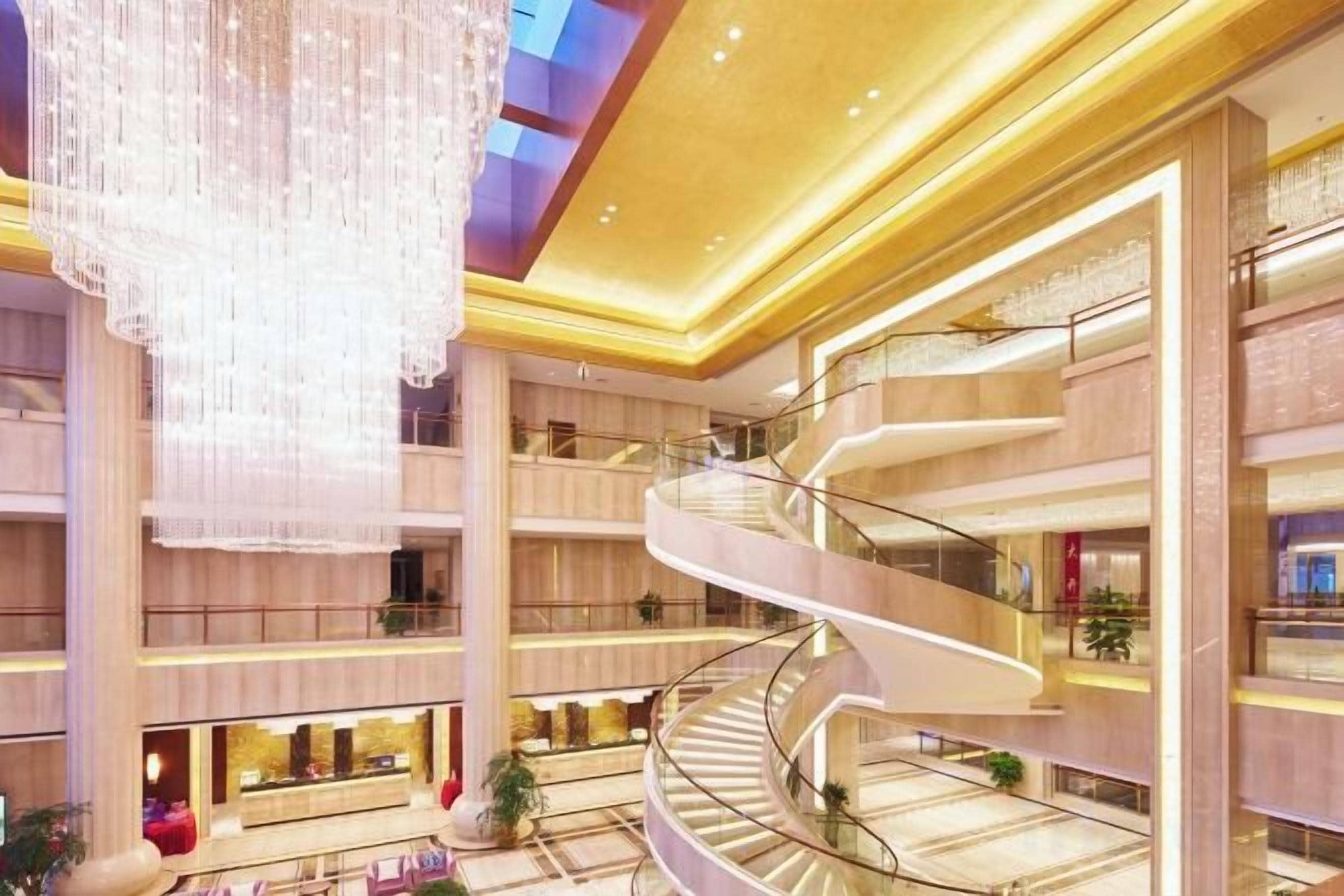 Un atrio de varios niveles con una escalera espiral central, grandes candelabros y múltiples pisos con locales comerciales.