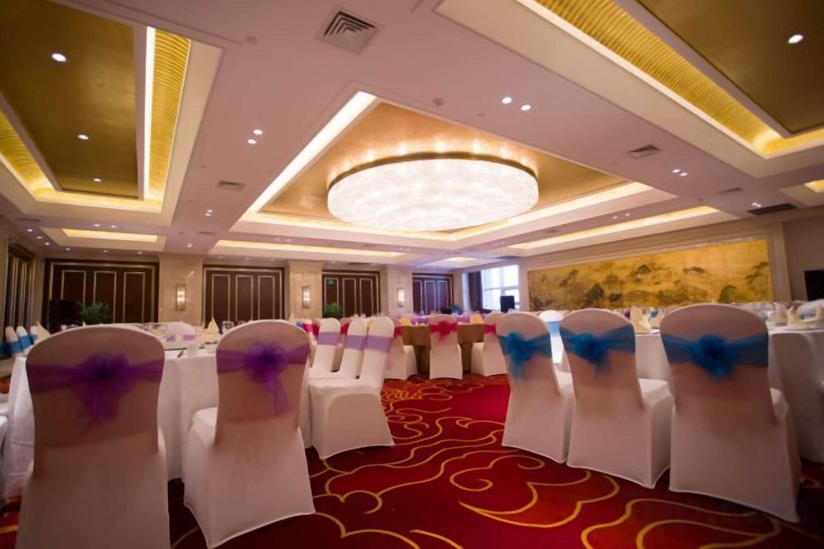 Une salle de banquet avec des tables rondes et des chaises, un tapis rouge et un grand lustre.