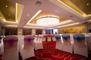 A banquet hall with round tables and chairs, a red carpet, and a large chandelier.